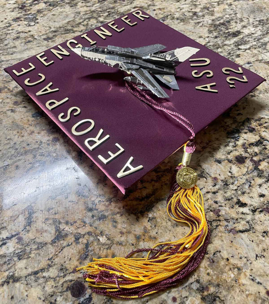 Mortarboard decorations by Isiah Udasco, aerospace engineering BSE, that includes a 3D jet model and the words "Aerospace Engineering ASU '22."