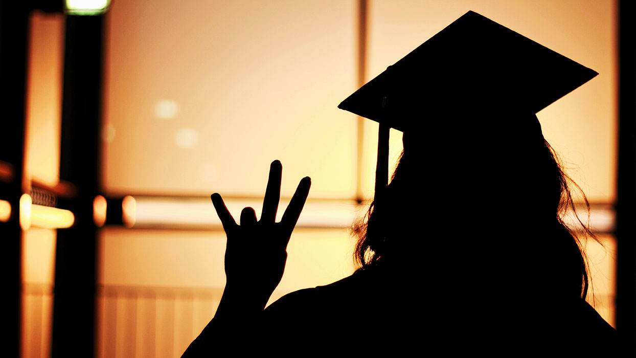 Silhouette of a student in a graduation cap making the fork symbol with their hand