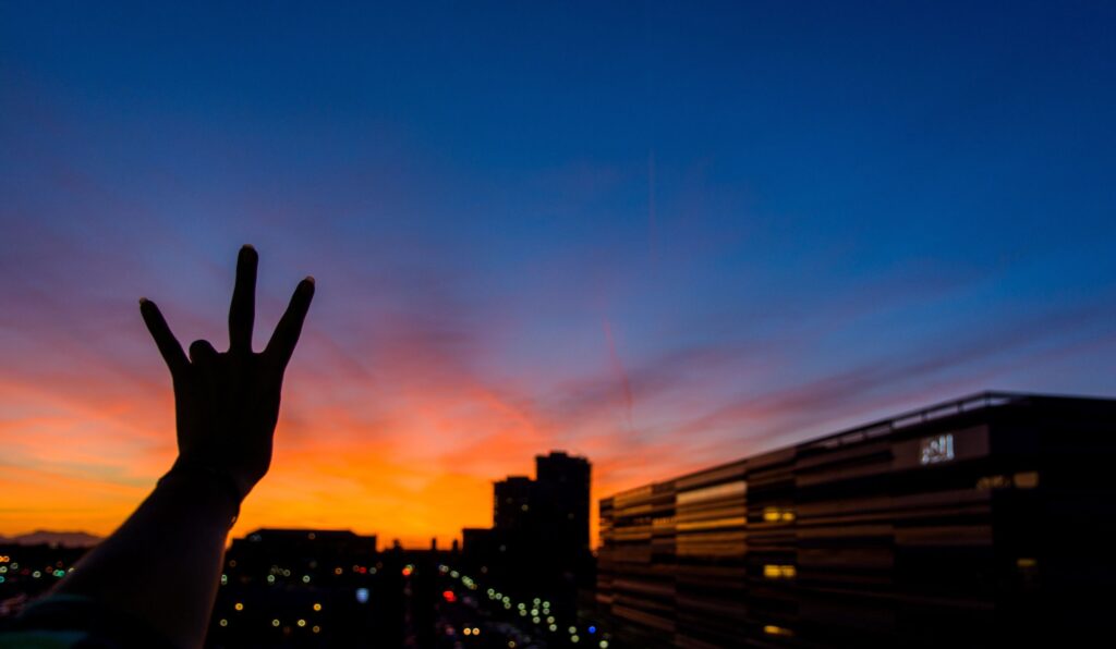 Tempe campus skyline at night with a hand holding up the fork symbol