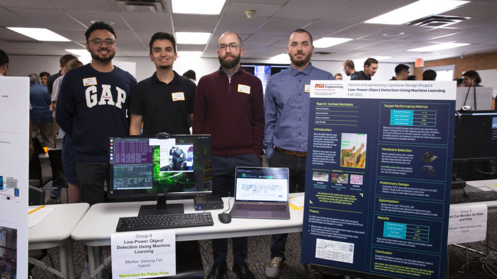 Students stand in front of their capstone presentation project at a Demo Day event.