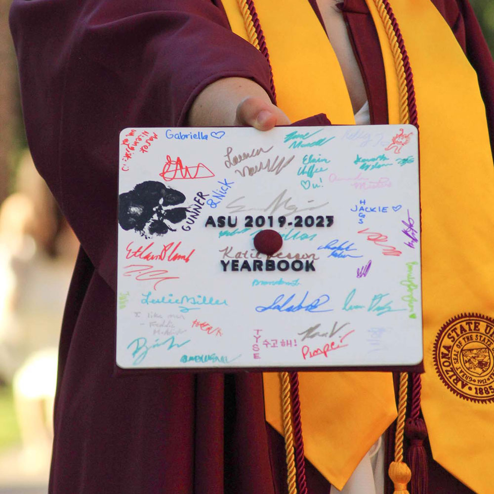 A mortarboard themed after a yearbook for 2019-2023 full of signatures.