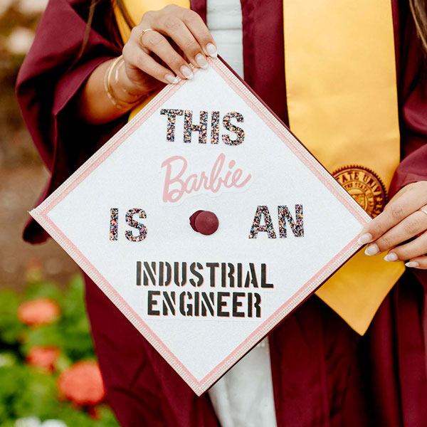 A decorated mortarboard in pink, white and glitter that says "This Barbie is an industrial engineer."