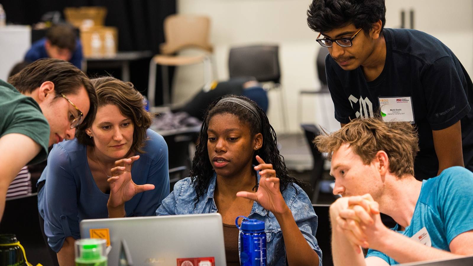Group of students and mentor sitting around an open laptop having an active discussion.