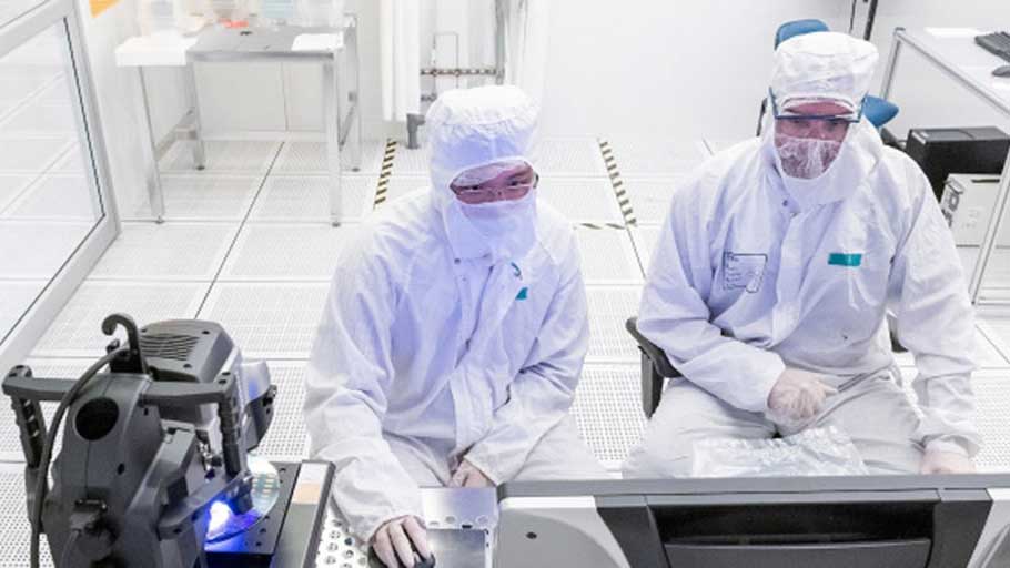 Two lab workers in white lab outfits working on a machine.